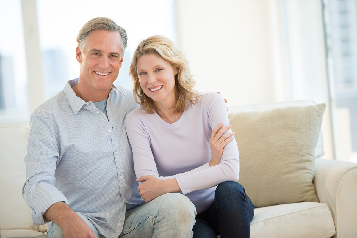 middle-aged couple sitting on beige couch, smiling